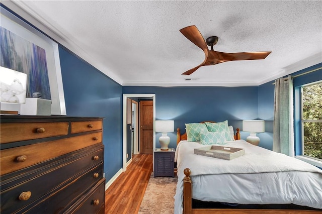 bedroom featuring crown molding, a textured ceiling, visible vents, and wood finished floors