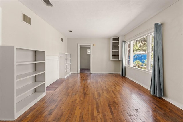 unfurnished living room with wood-type flooring, visible vents, and baseboards