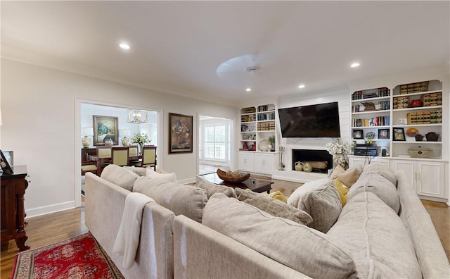 living room featuring crown molding, ceiling fan with notable chandelier, built in features, and light wood-type flooring