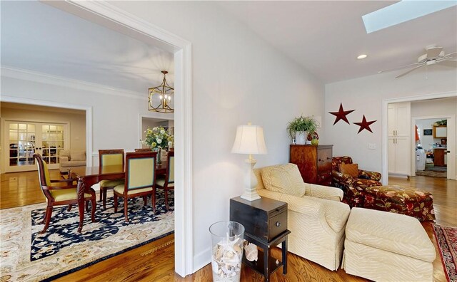 living room with hardwood / wood-style flooring, crown molding, ceiling fan with notable chandelier, and a skylight