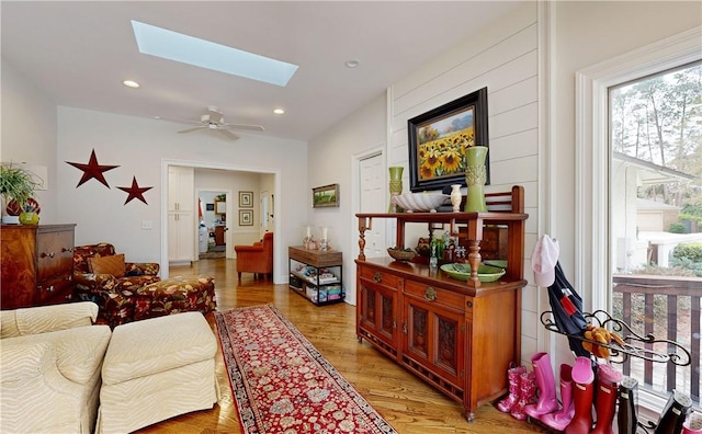 living room with ceiling fan, a skylight, and light hardwood / wood-style flooring