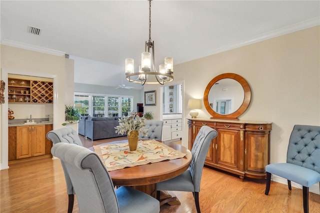 dining room featuring visible vents, light wood-style flooring, ornamental molding, a chandelier, and indoor wet bar