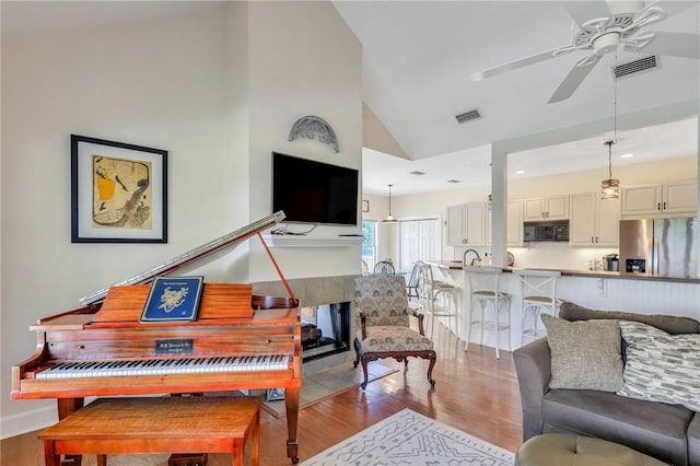 living area with light wood finished floors, a tiled fireplace, visible vents, and a ceiling fan