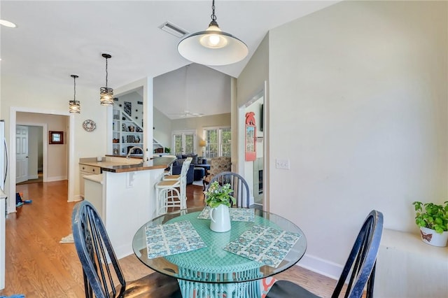 dining space featuring vaulted ceiling, light wood-type flooring, visible vents, and baseboards