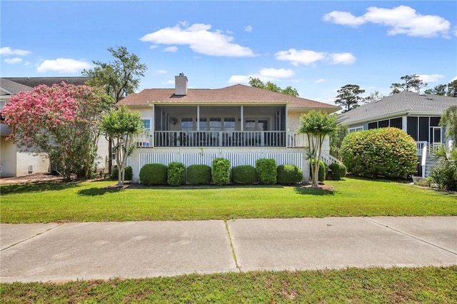 view of front of home with a front yard, a sunroom, and a chimney