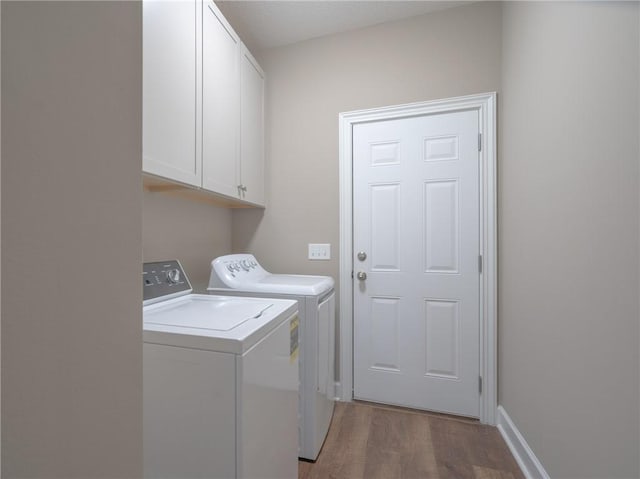 washroom featuring hardwood / wood-style flooring, washer and clothes dryer, and cabinets