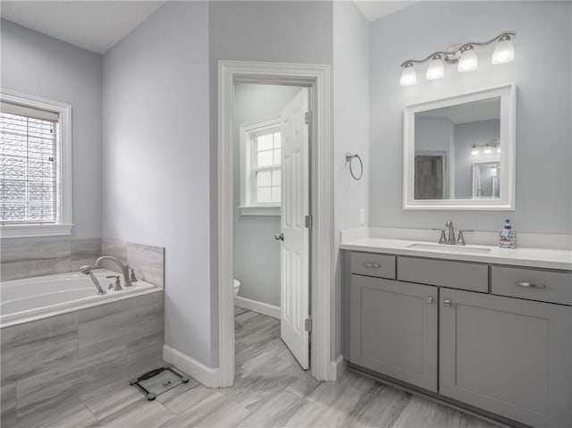 bathroom featuring vanity, a relaxing tiled tub, a wealth of natural light, and toilet