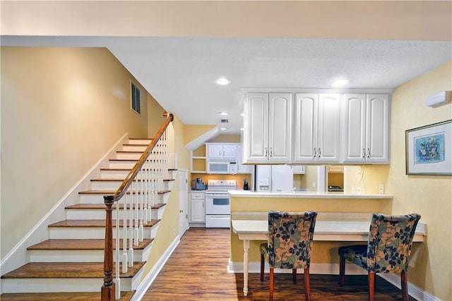 kitchen with white appliances, wood-type flooring, white cabinets, a kitchen bar, and kitchen peninsula