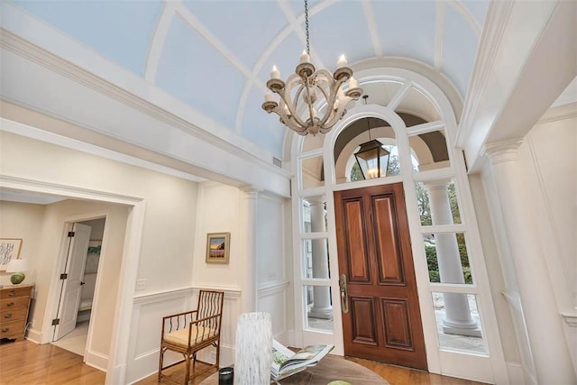 entryway featuring a decorative wall, an inviting chandelier, vaulted ceiling, wood finished floors, and ornate columns