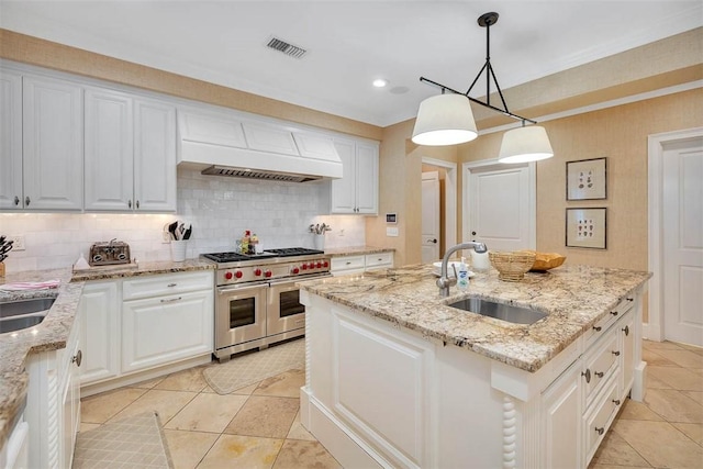 kitchen featuring visible vents, a kitchen island with sink, premium range hood, double oven range, and a sink