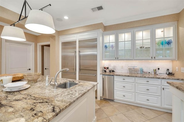 kitchen featuring visible vents, glass insert cabinets, a sink, white cabinetry, and backsplash