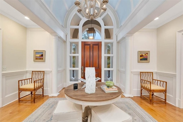 living area with ornate columns, a decorative wall, wood finished floors, and an inviting chandelier