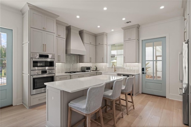 kitchen featuring premium range hood, a kitchen island, light hardwood / wood-style floors, and a kitchen breakfast bar