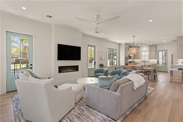 living room with ceiling fan, ornamental molding, and light wood-type flooring