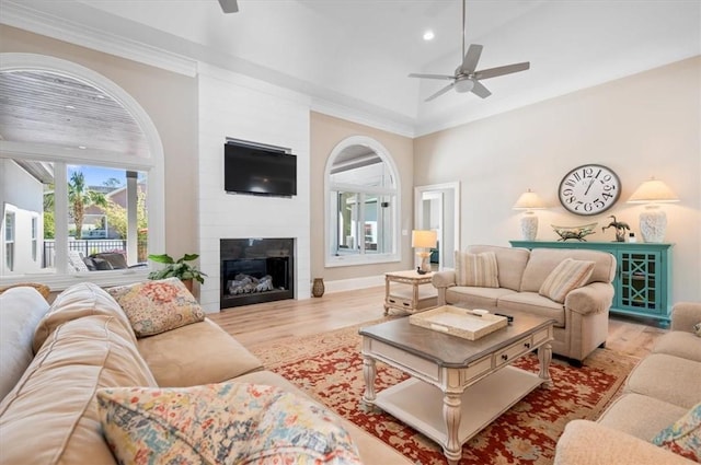 living room with ornamental molding, a large fireplace, vaulted ceiling, ceiling fan, and wood-type flooring