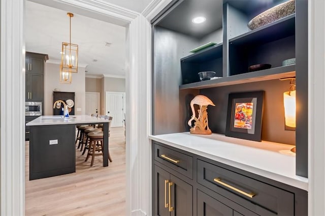 bar featuring stainless steel microwave, sink, light hardwood / wood-style flooring, decorative light fixtures, and ornamental molding