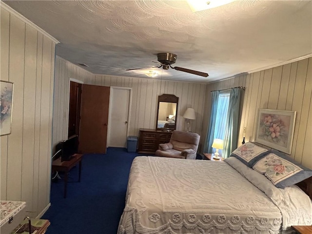 bedroom with ceiling fan, wooden walls, and dark colored carpet