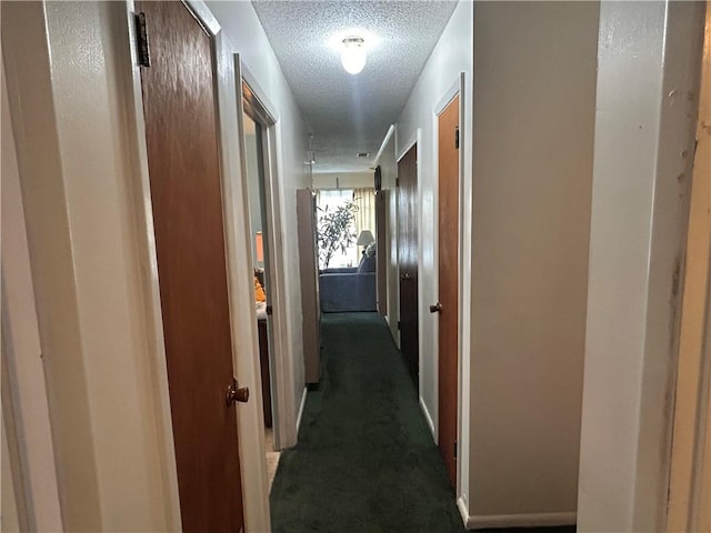 hallway with a textured ceiling and dark carpet