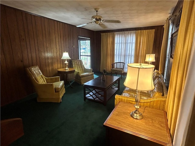 sitting room featuring wood walls, ceiling fan, and dark colored carpet