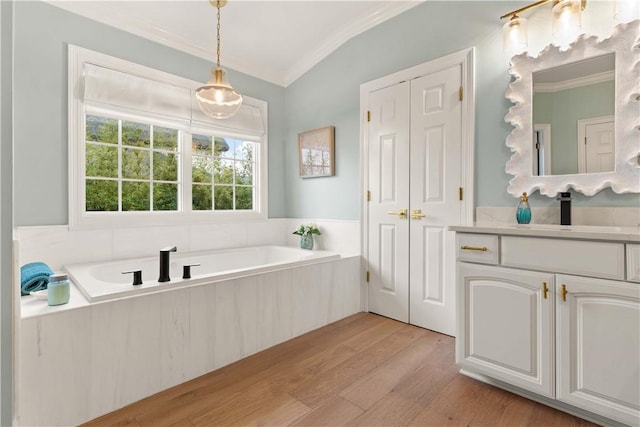 bathroom featuring a garden tub, wood finished floors, vanity, vaulted ceiling, and ornamental molding