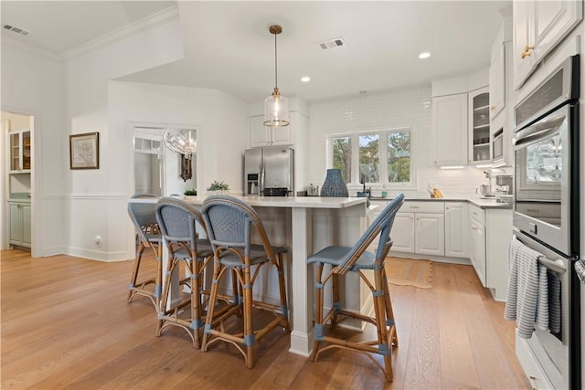 kitchen with a center island, visible vents, appliances with stainless steel finishes, white cabinets, and a kitchen bar