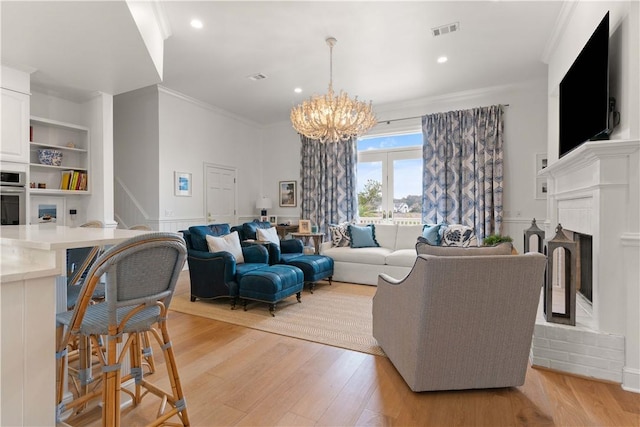 living area featuring visible vents, a fireplace with raised hearth, ornamental molding, an inviting chandelier, and light wood-type flooring