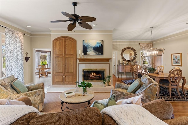 living room featuring a tiled fireplace, ornamental molding, ceiling fan with notable chandelier, and light hardwood / wood-style flooring