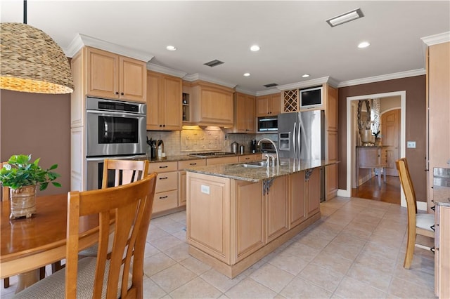 kitchen with sink, hanging light fixtures, stainless steel appliances, light stone countertops, and a center island with sink