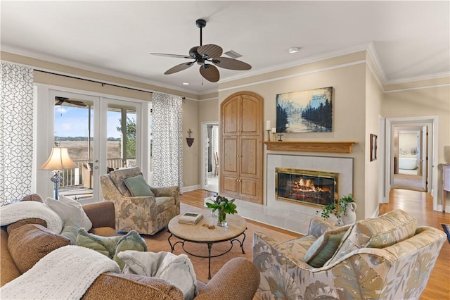 living room featuring ornamental molding, a tile fireplace, french doors, and light wood-type flooring