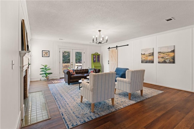 living room with a notable chandelier, a textured ceiling, french doors, dark hardwood / wood-style flooring, and a barn door