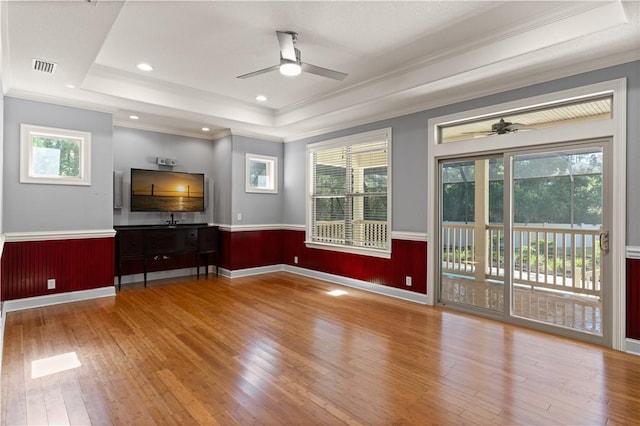 unfurnished living room with light hardwood / wood-style floors, ornamental molding, and a tray ceiling