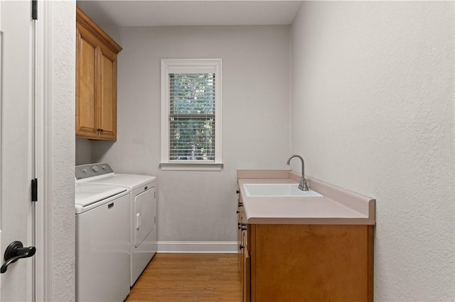 laundry room featuring separate washer and dryer, sink, cabinets, and light hardwood / wood-style flooring