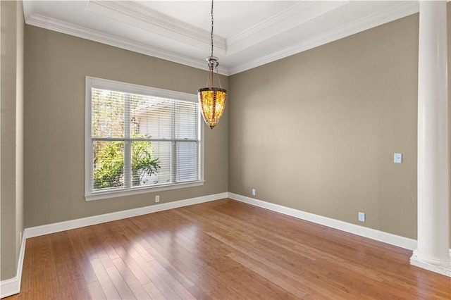 unfurnished room with a raised ceiling, crown molding, hardwood / wood-style flooring, ornate columns, and a notable chandelier