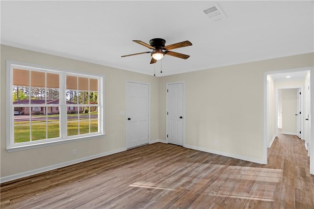 empty room featuring visible vents, ceiling fan, wood finished floors, and baseboards