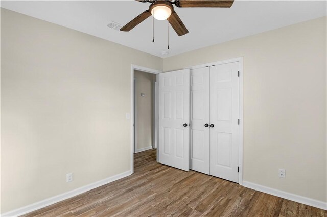 unfurnished bedroom with a closet, baseboards, visible vents, ceiling fan, and wood finished floors