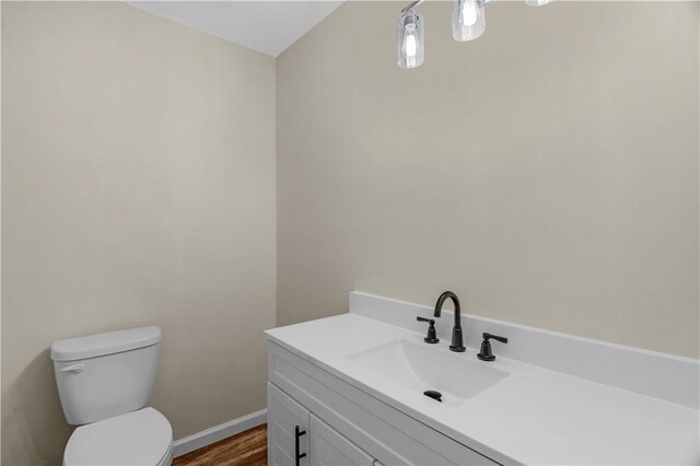bathroom with toilet, vanity, wood finished floors, and baseboards