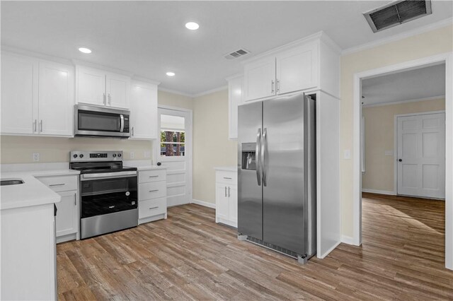 kitchen featuring stainless steel appliances, visible vents, ornamental molding, and light wood-style flooring