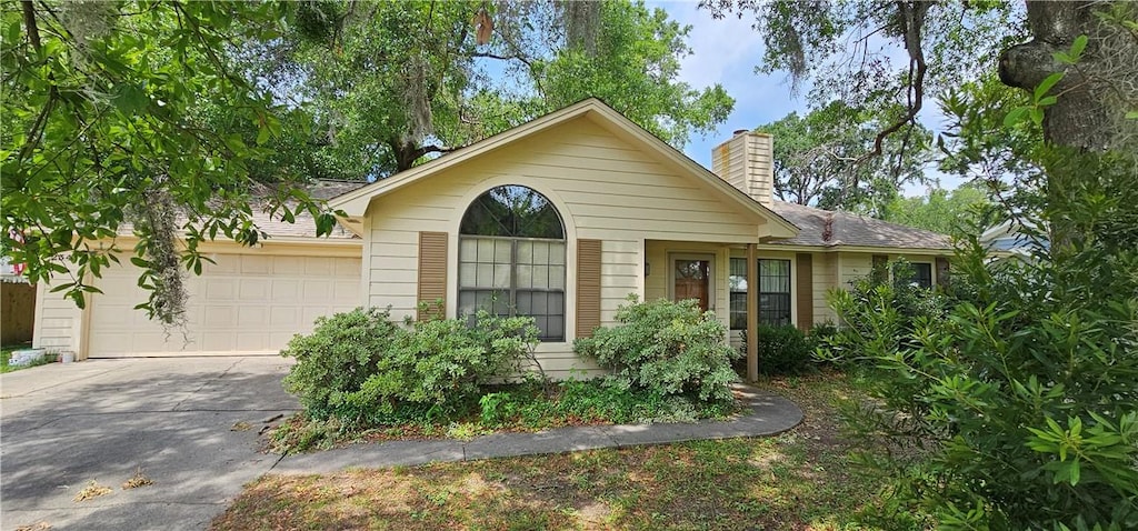 single story home featuring driveway, a chimney, and a garage