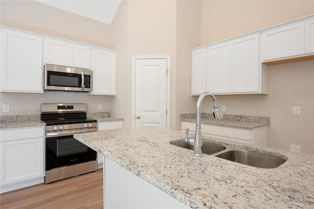 kitchen with light stone counters, a sink, light wood-style floors, white cabinets, and appliances with stainless steel finishes