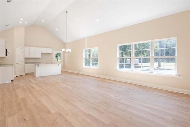 unfurnished living room with baseboards, high vaulted ceiling, light wood-type flooring, and an inviting chandelier