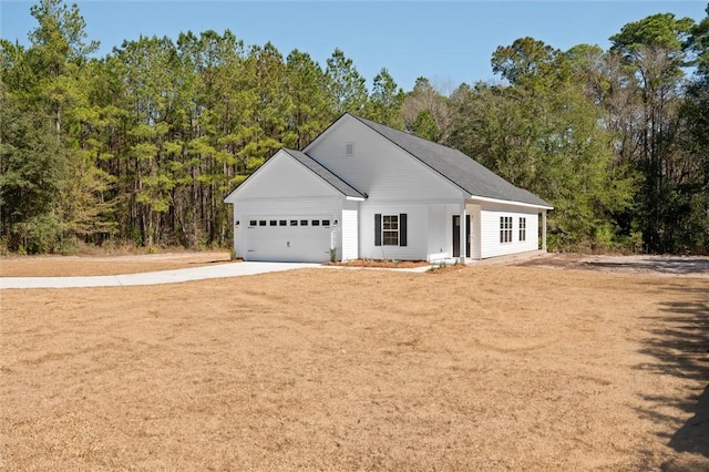 single story home with a garage, concrete driveway, and a forest view