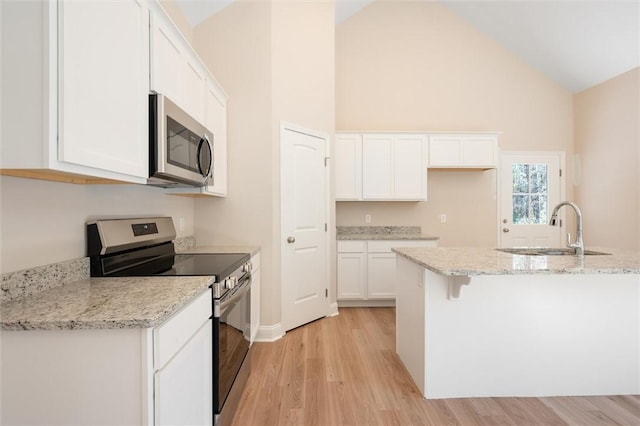 kitchen with white cabinets, light wood-style flooring, appliances with stainless steel finishes, light stone countertops, and a sink