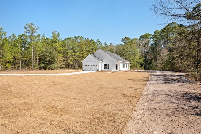 view of front of home featuring a front yard, an attached garage, driveway, and a forest view