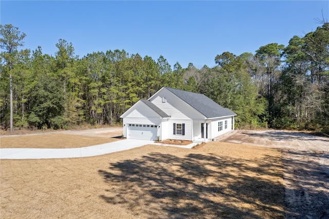 view of front facade with concrete driveway, an attached garage, and a forest view