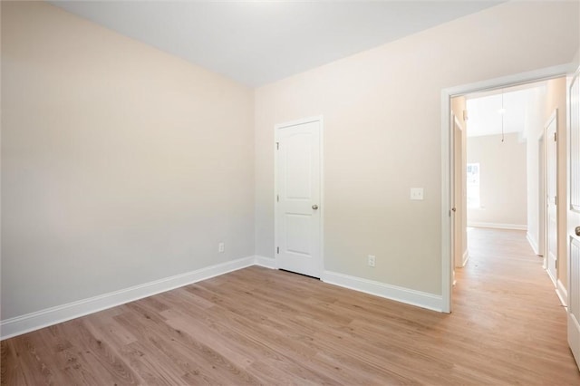 unfurnished room with baseboards, attic access, and light wood-style floors