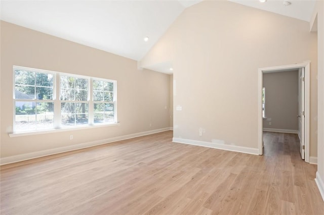 empty room with light wood finished floors, baseboards, and high vaulted ceiling