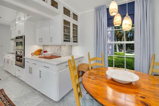 kitchen with backsplash, white cabinetry, stainless steel double oven, and decorative light fixtures