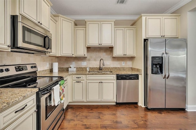 kitchen featuring appliances with stainless steel finishes, sink, crown molding, light stone countertops, and cream cabinetry