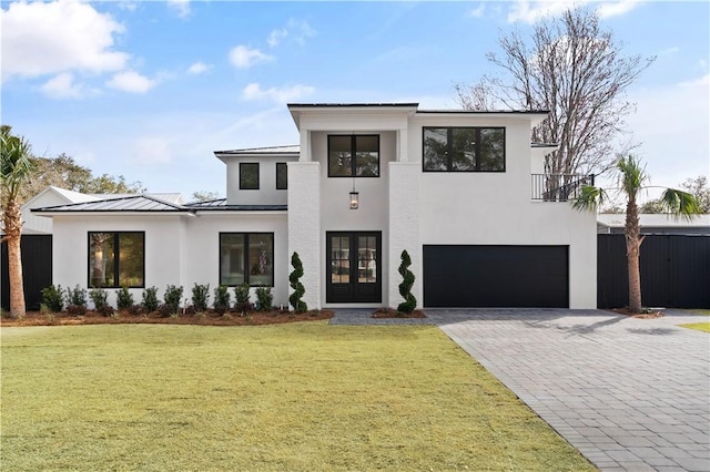 modern home featuring a front lawn, a garage, a standing seam roof, decorative driveway, and french doors