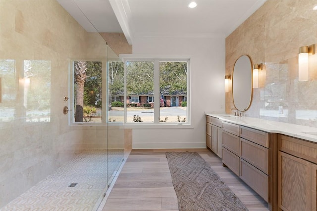 bathroom featuring double vanity, a shower, wood finished floors, a sink, and baseboards